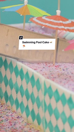 From Deadpool to swimming pool! 🏊‍♀️ 🌊 This is a cake for all the Leos in your life! Whether you're attending a ♌️ birthday, pool party or another summer celebration this month, this swimming pool cake complete with royal icing tiles, gumpaste pool liner, jello water, sprinkle shinmering sand, chocolate daybeds and tables, and fruit inspired cocktail umbrellas is sure to make a SPLASH! 💦 Full recipe in our brand new YouTube video! #cake #cakedecorating #howtocakeit #recipe #summer #summervibe