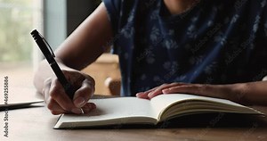 Close up African woman sit at table keeping her personal diary, holding pen writes down in notepad important event and activities, create to-do list. Studying process, vent feelings on paper concept