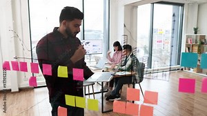 Business team collaborating on project using sticky notes and laptop in modern office. Young professionals discussing ideas and planning strategy during brainstorming session.