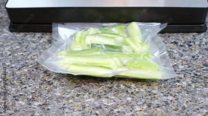 Process of packing cucumbers in bag using vacuum machine on a gray background.