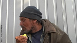 Homeless man with toothless mouth trying to eat an apple. 50 year old wretched beggar living on the streets for 20 years.